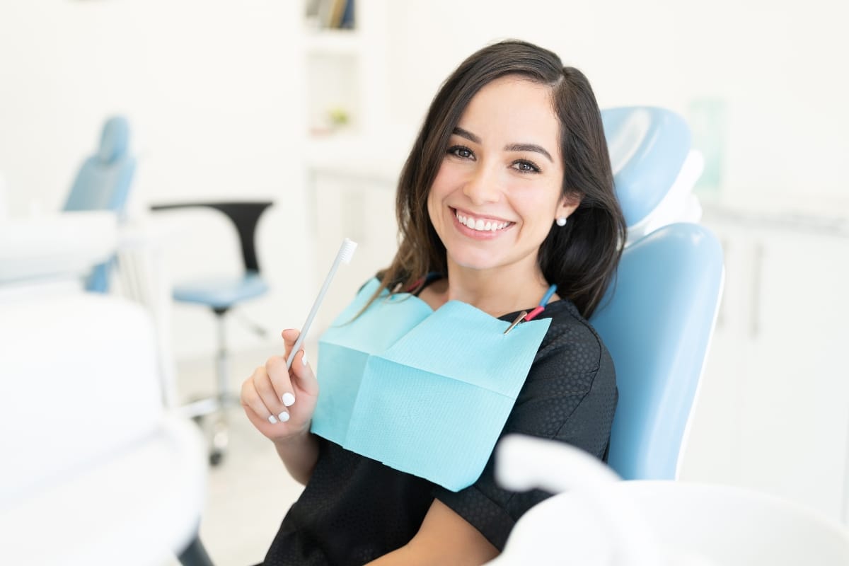 Smiling woman in a dental clinic holding a toothbrush for smile design services.